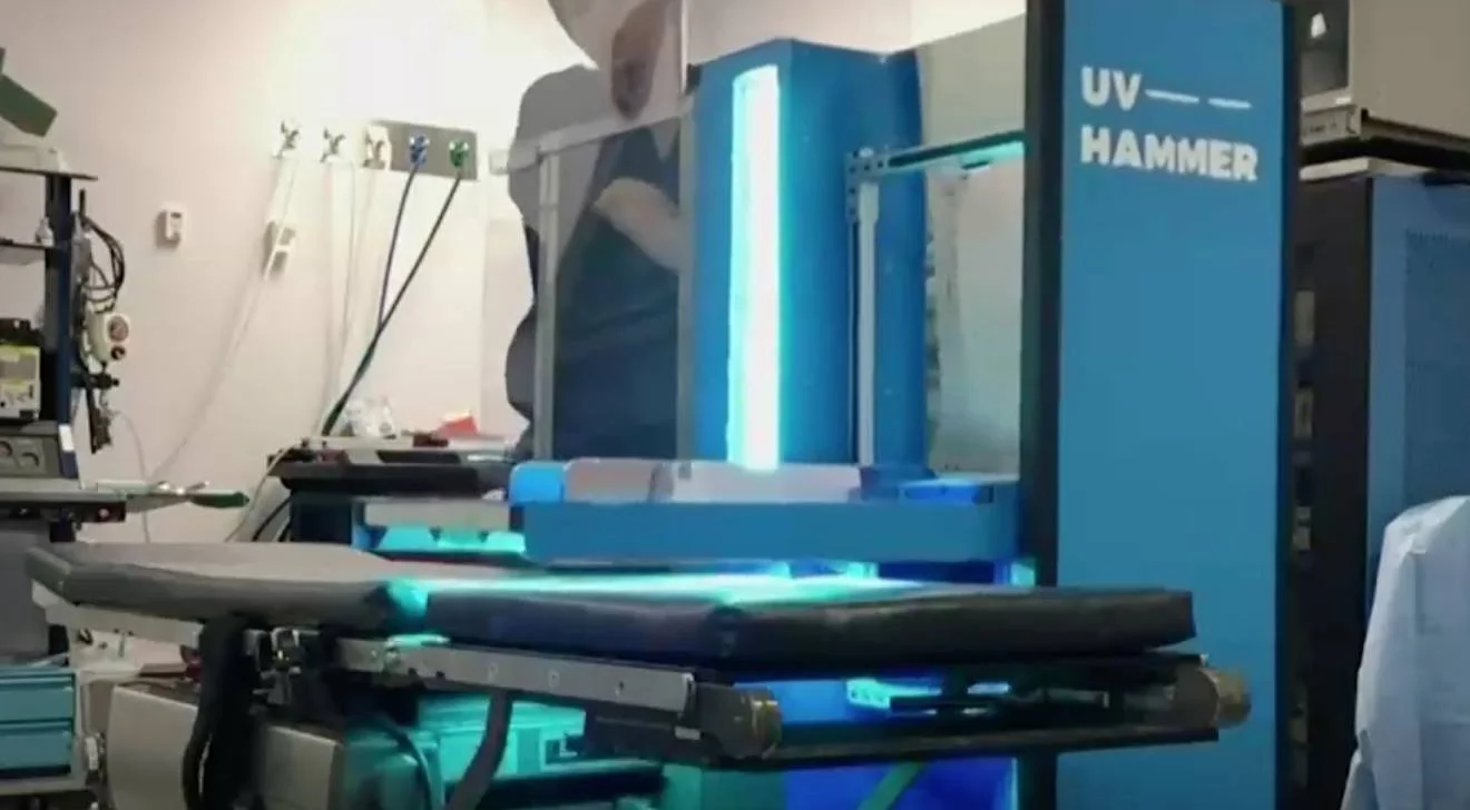 Técnico opera una máquina de luz ultravioleta UV Hammer de color azul en un laboratorio industrial.