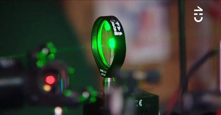 Espejo óptico circular iluminado por un haz láser verde en un laboratorio de física experimental.