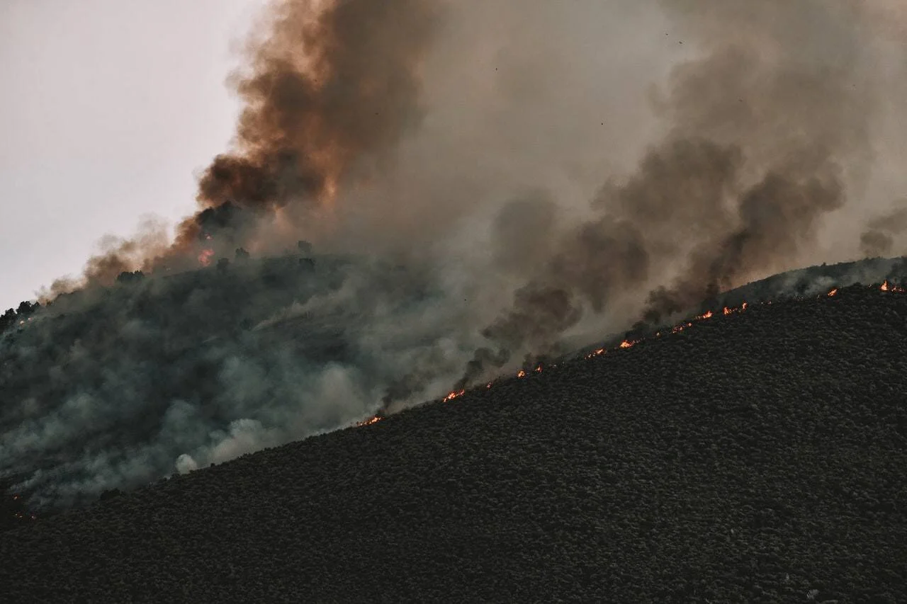 Llamas y columnas de humo denso consumen la vegetación de una ladera montañosa durante un incendio forestal.