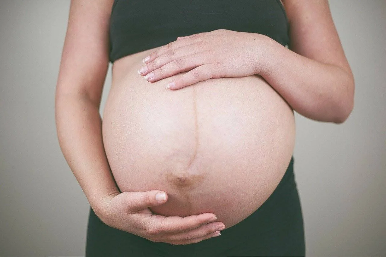 Mujer embarazada en avanzado estado de gestación sostiene su vientre con ambas manos.