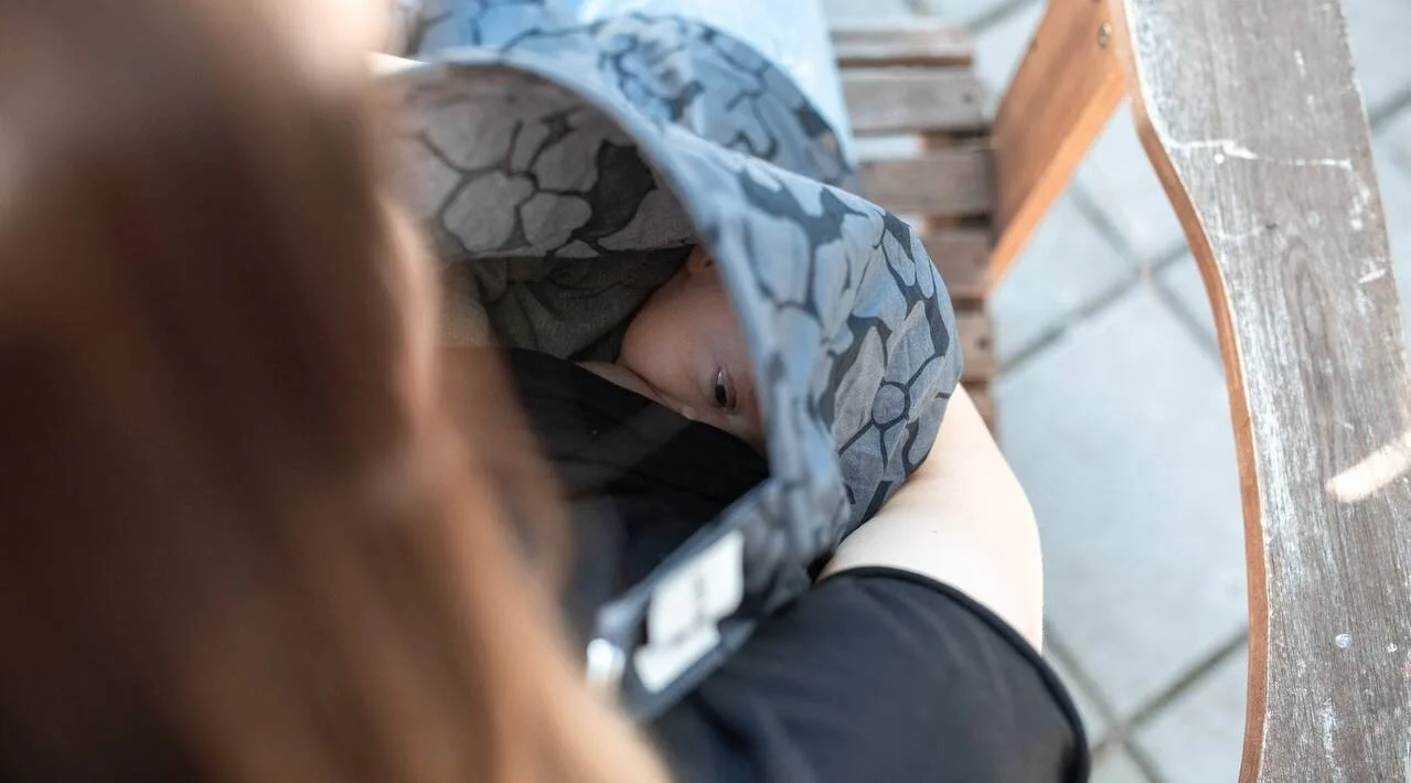 Una madre amamanta a su bebé en público cubierta con una manta estampada en gris.
