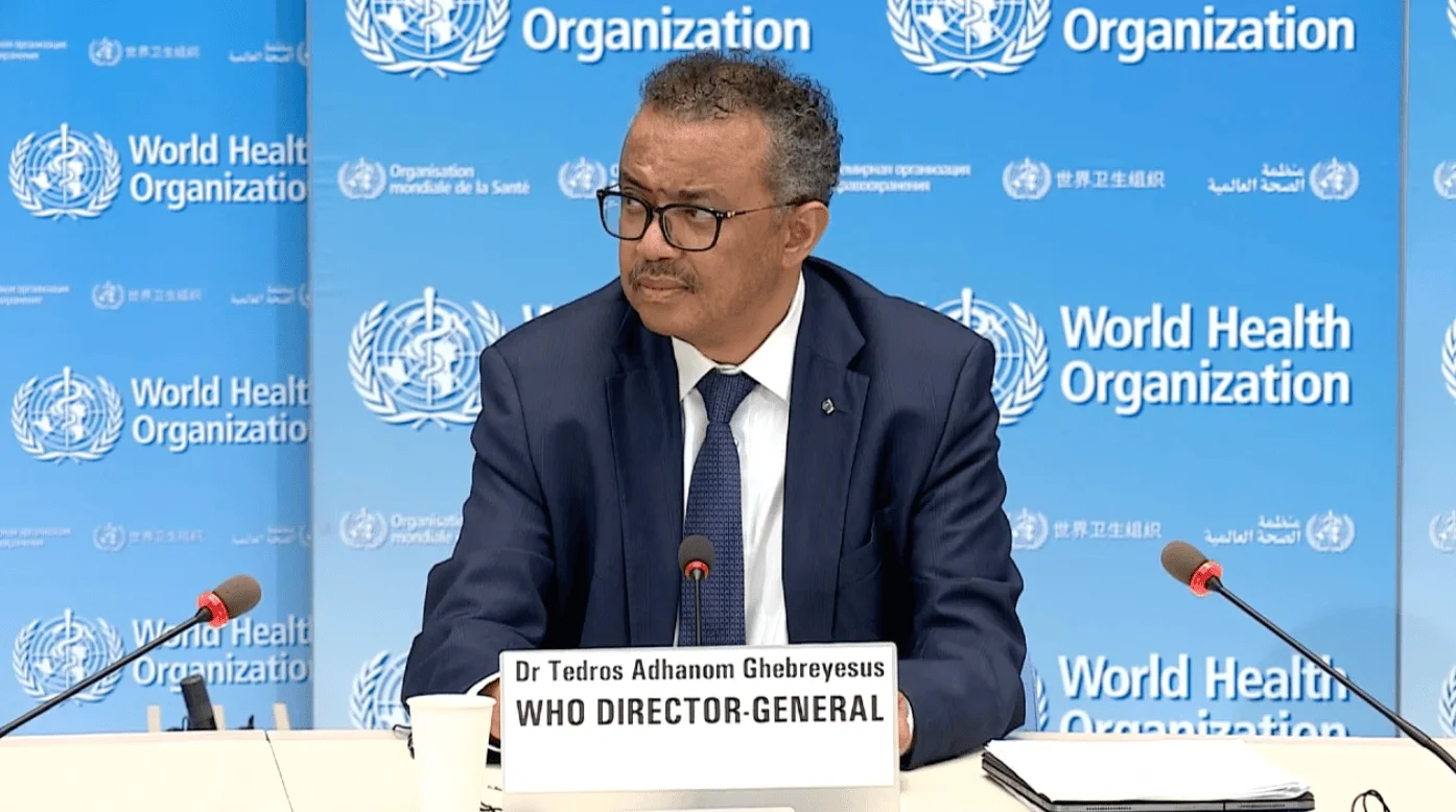 El Dr. Tedros Adhanom Ghebreyesus, Director General de la OMS, habla ante micrófonos frente al panel institucional de la organización.