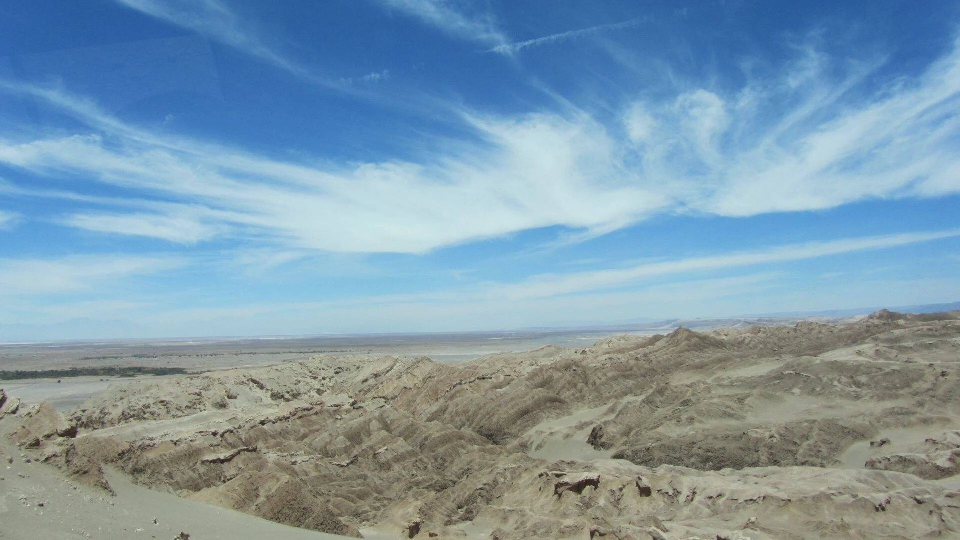 Vasta llanura desértica con formaciones rocosas erosionadas bajo un cielo azul con nubes cirros.
