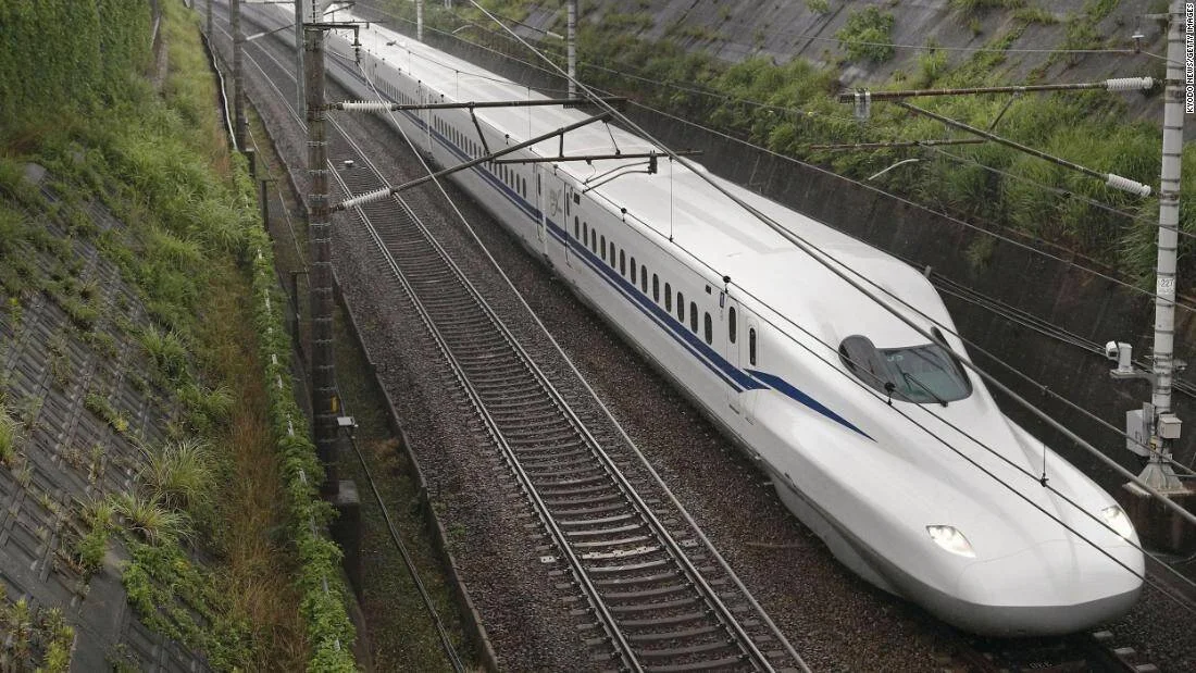 Tren de alta velocidad Shinkansen de color blanco con franja azul avanza por una vía rodeada de vegetación en Japón.