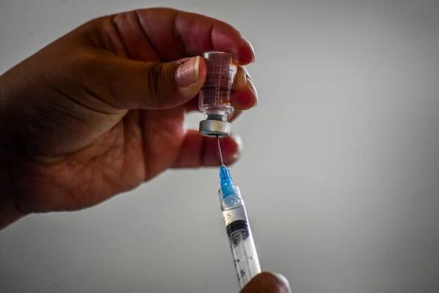 Una mano sostiene un frasco de vacuna mientras extrae la dosis con una jeringa.