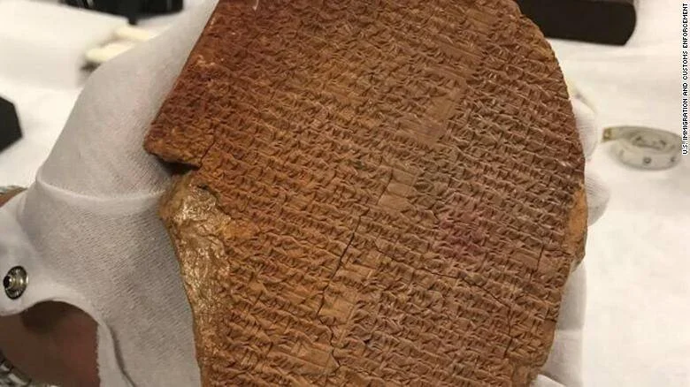 Manos con guantes blancos sostienen una tablilla de arcilla con inscripciones cuneiformes antiguas, confiscada por el Servicio de Inmigración y Control de Aduanas de EE.UU.