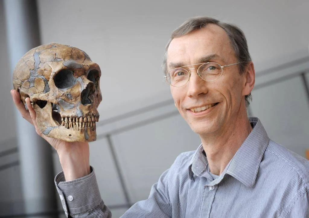 Investigador con gafas sostiene en alto un cráneo fósil de neandertal y sonríe a la cámara.