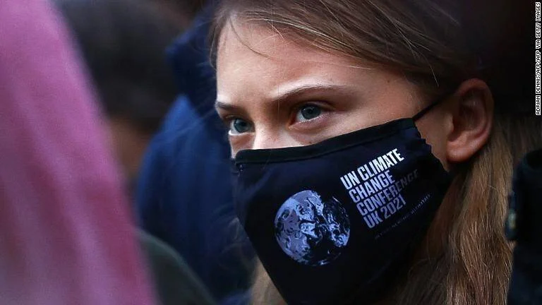 Joven con mascarilla negra de la Conferencia de Cambio Climático de la ONU UK 2021 entre una multitud.