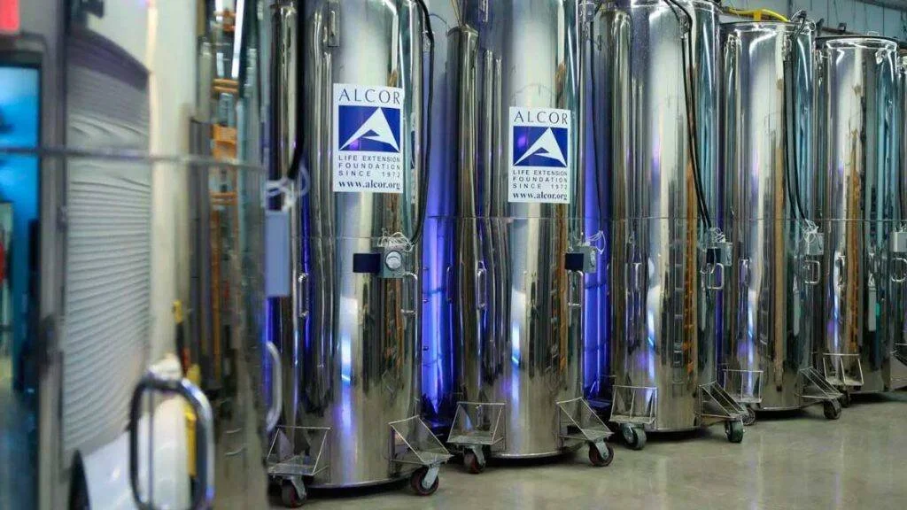 Fila de tanques metálicos criogénicos con el logo de Alcor Life Extension Foundation en una instalación industrial.