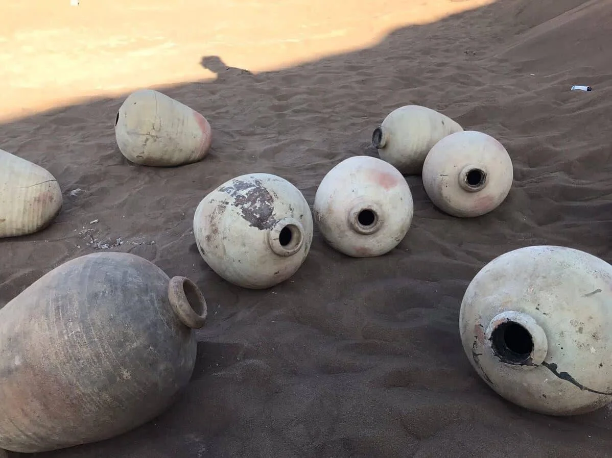 Varias vasijas y ánforas de cerámica antigua, deterioradas, dispersas sobre arena del desierto.