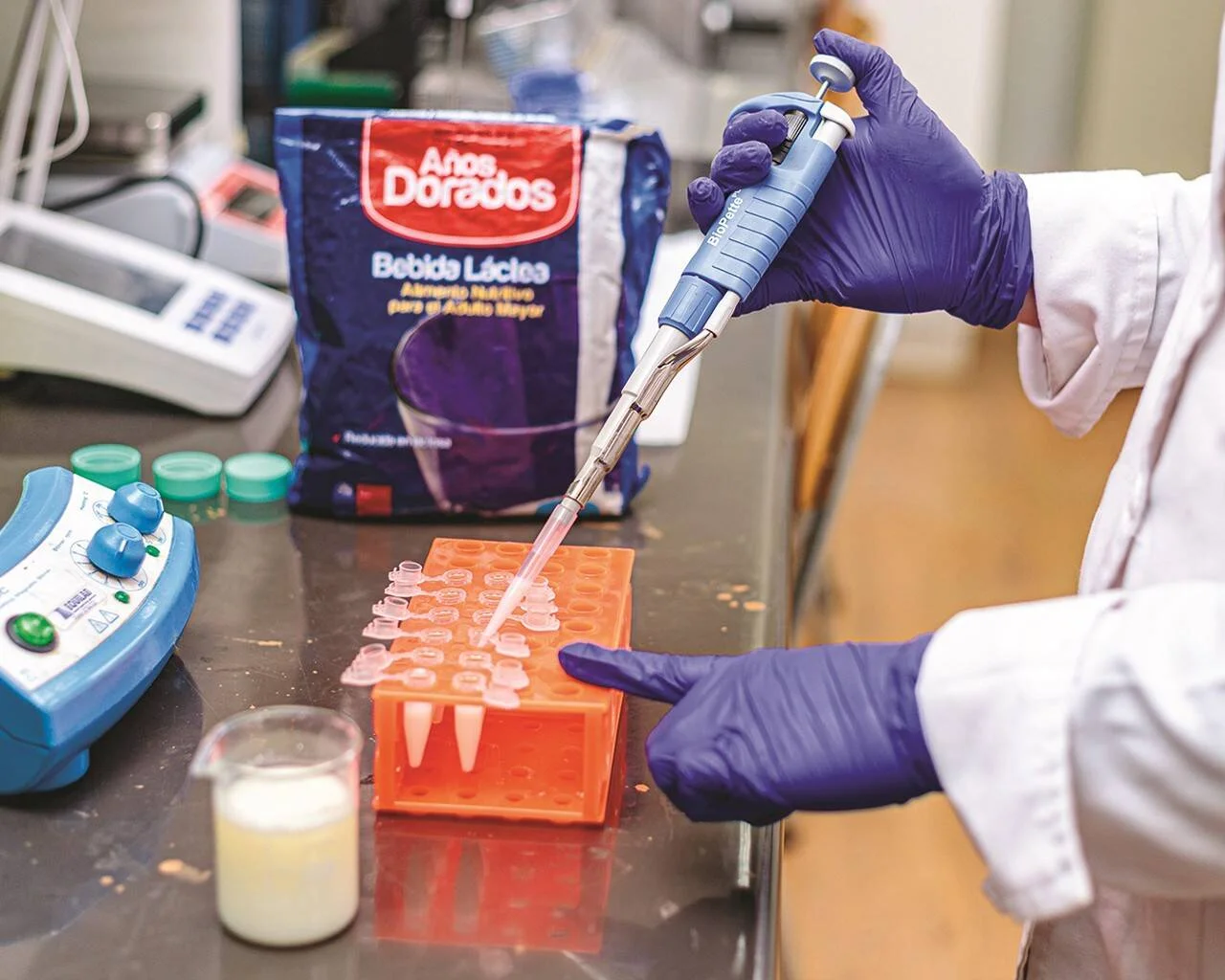 Técnico de laboratorio pipetea muestras junto a un envase de bebida láctea Años Dorados para adultos mayores.