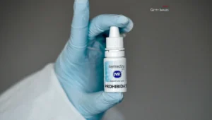 Mano con guante médico azul sostiene un frasco de ivermectina con la leyenda 'PROHIBIDA' en su etiqueta.