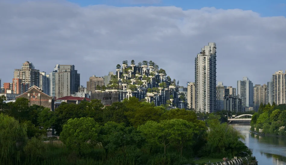 Edificio de diseño escalonado cubierto de árboles y vegetación integrado en el horizonte de una ciudad junto a un río.