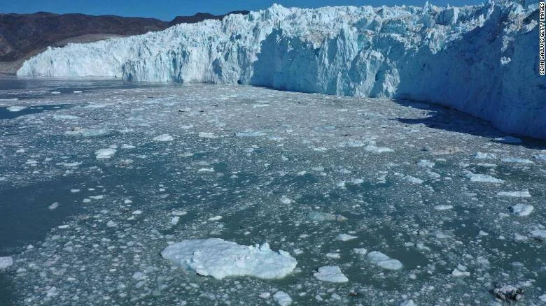Frente de un glaciar desprendiendo bloques de hielo que flotan en el mar bajo un cielo despejado.