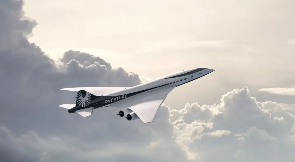 Renderizado del avión supersónico Overture volando entre nubes, con su diseño aerodinámico blanco y negro característico.