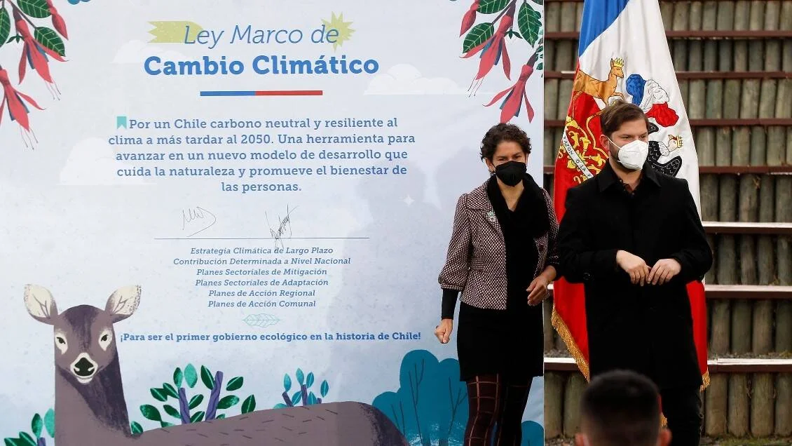 Dos autoridades con mascarilla frente al cartel de la Ley Marco de Cambio Climático de Chile y la bandera nacional.