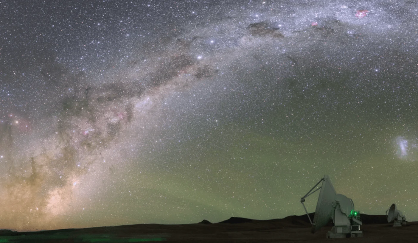 El arco completo de la Vía Láctea se extiende sobre el horizonte desértico donde se siluetean antenas de radiotelescopios.
