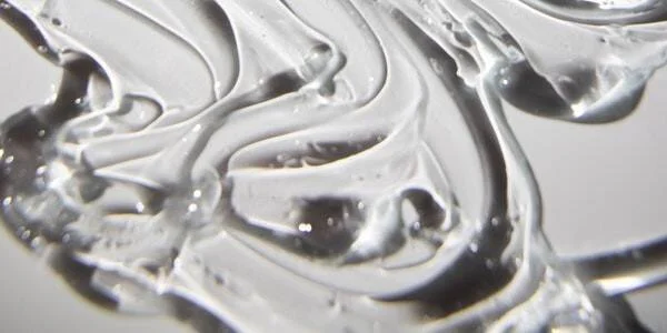 Primer plano de una sustancia gel transparente con ondas y burbujas diminutas sobre fondo claro.