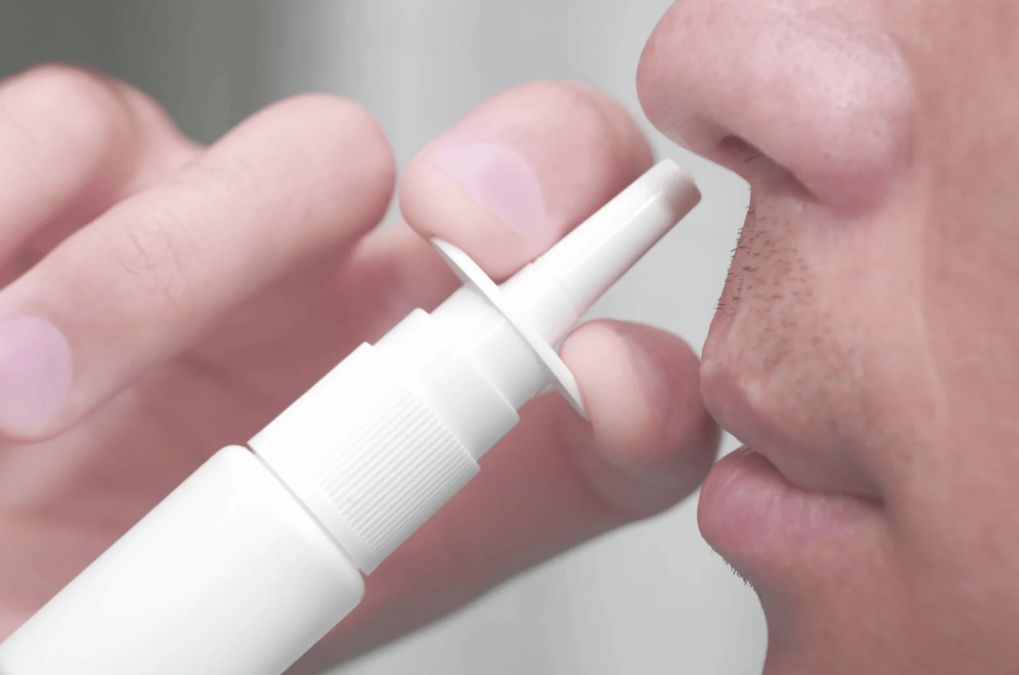 Una persona se aplica un spray nasal blanco en la fosa nasal con los dedos.