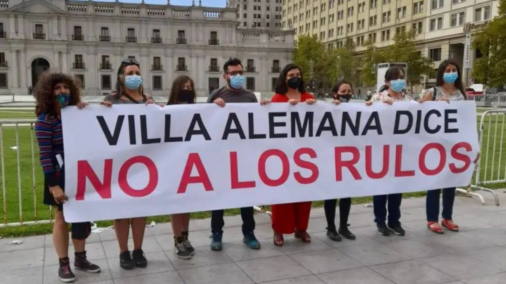 Grupo de personas con mascarillas sostiene una pancarta que dice 'Villa Alemana dice NO A LOS RULOS' frente a La Moneda, Santiago de Chile.