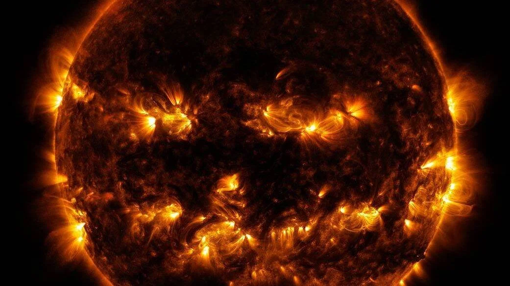 El Sol fotografiado en luz ultravioleta extrema muestra brillantes erupciones y bucles de plasma sobre su superficie oscurecida.