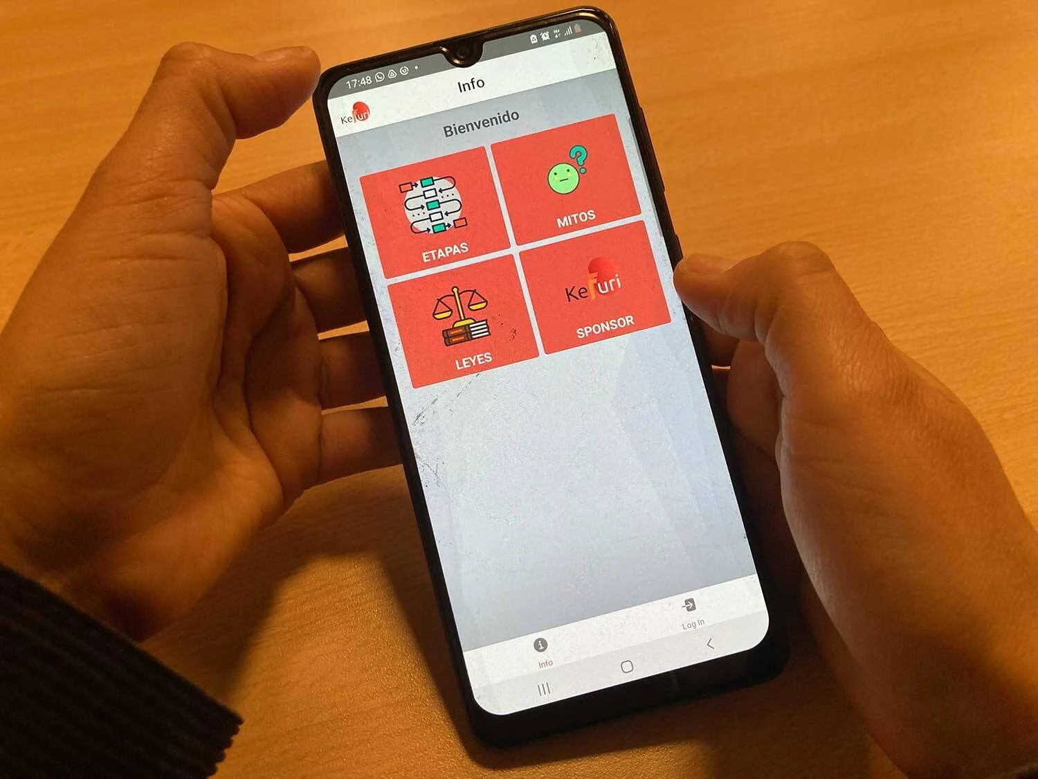 Manos sosteniendo un teléfono con la app Kefuri abierta, mostrando secciones de Etapas, Mitos, Leyes y Sponsor.