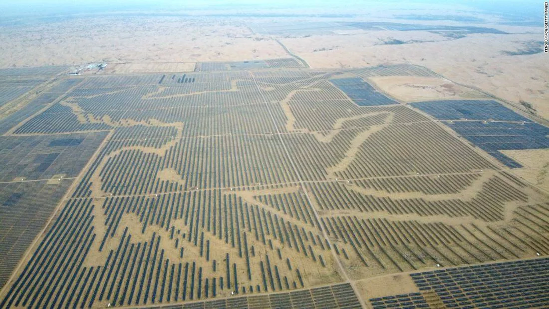 Vista aérea de una vasta planta de paneles solares fotovoltaicos dispuestos en patrones sobre terreno desértico árido.