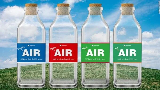Cuatro botellas de vidrio con tapón de corcho que contienen aire etiquetado como escocés, inglés, galés e irlandés, sobre fondo de cielo y césped.