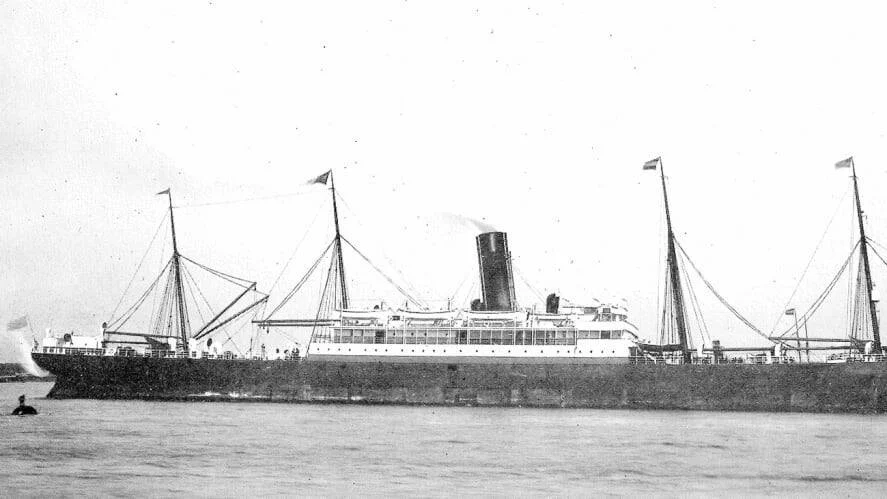 Fotografía histórica en blanco y negro de un gran barco de vapor con cuatro mástiles y una chimenea navegando en aguas tranquilas.