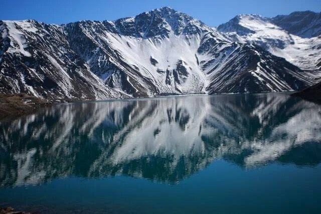 Lago de aguas turquesas reflejando montañas cubiertas de nieve bajo cielo azul despejado.