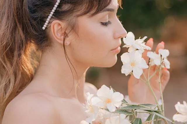 Mujer joven de perfil con diadema de perlas oliendo delicadas flores blancas silvestres.