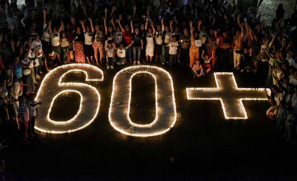 Multitud celebra la Hora del Planeta rodeando el símbolo '60+' formado con velas encendidas en el suelo durante la noche.