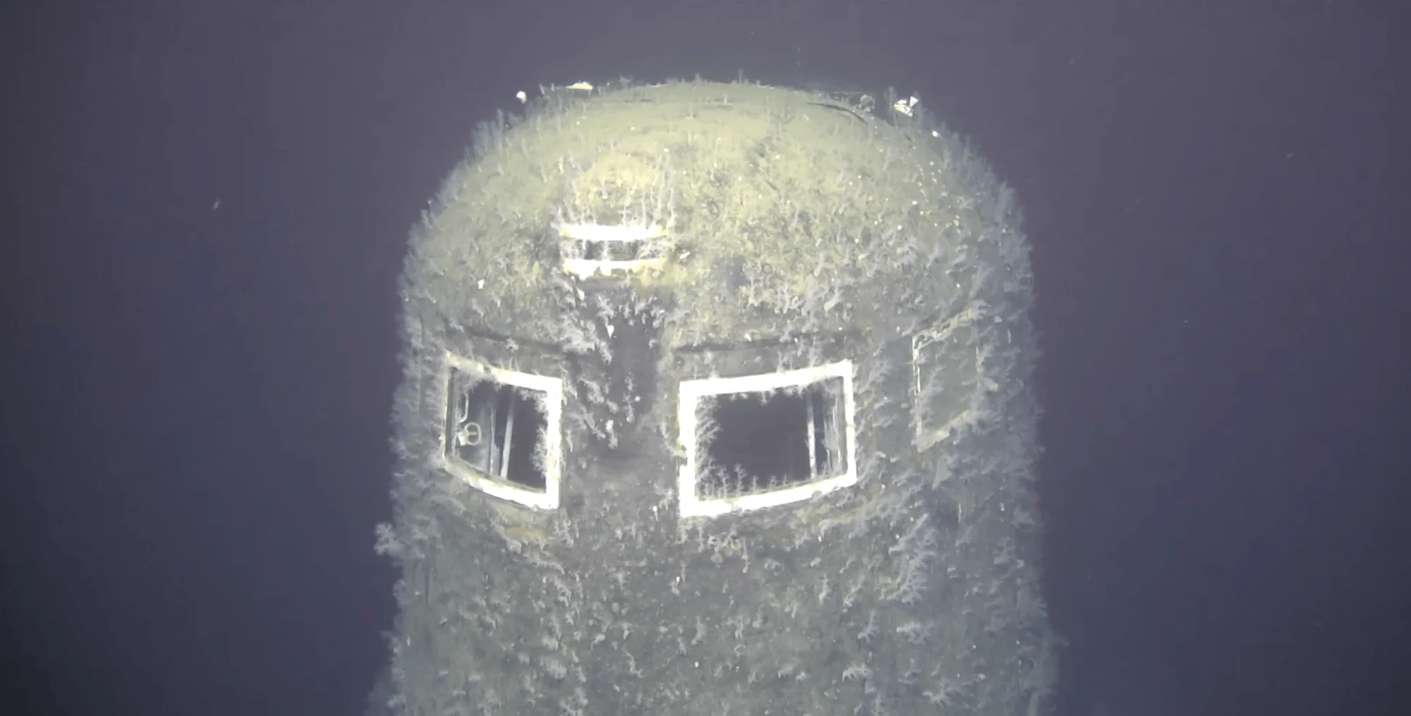 Torre de un submarino naufragado en el fondo del océano, completamente cubierta de incrustaciones marinas y corrosión.