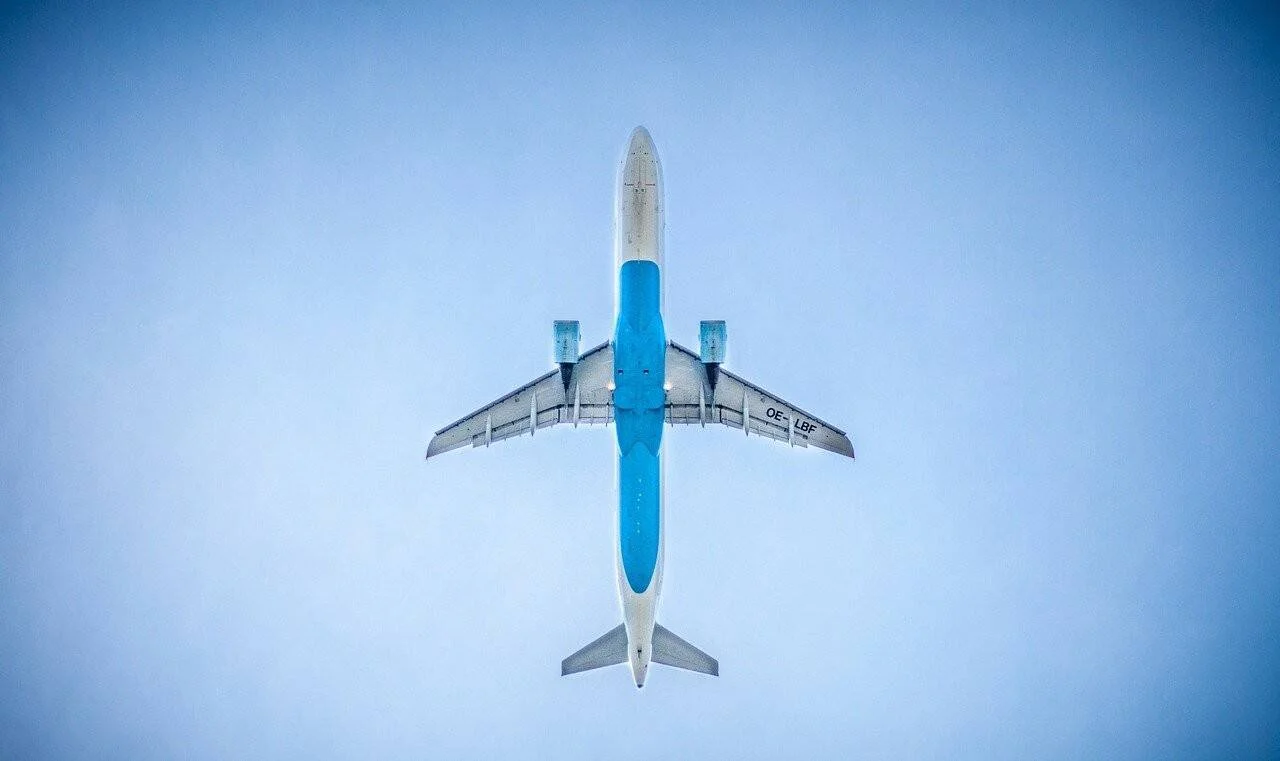 Avión de pasajeros con librea azul y blanca (matrícula OE-LBF) fotografiado desde tierra mientras sobrevuela el cielo.