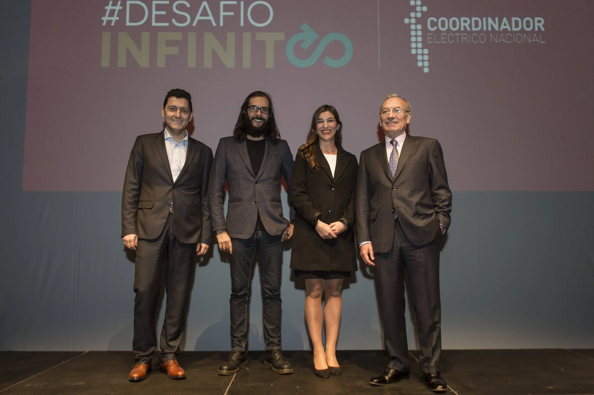 Cuatro personas posan ante una pantalla con el logo del evento #DesafíoInfinito del Coordinador Eléctrico Nacional.