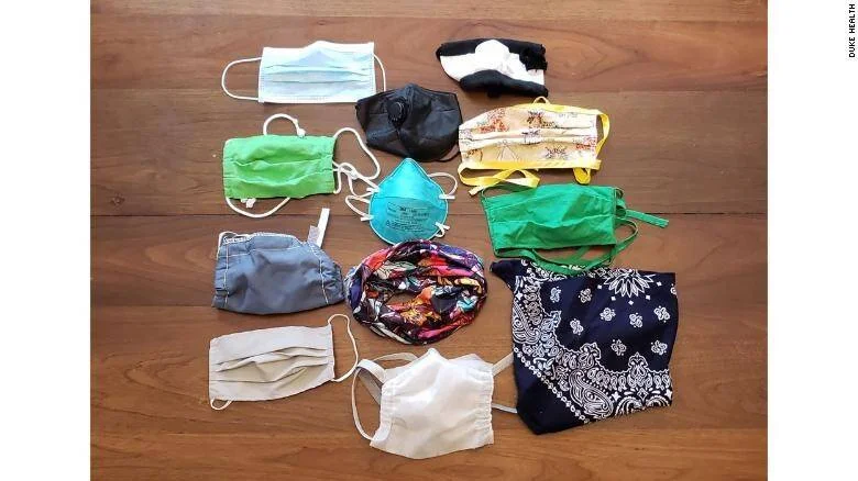 Colección de distintos tipos de mascarillas faciales, incluyendo quirúrgicas, N95, de tela y pañuelo, dispuestas sobre una superficie de madera.