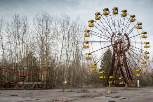 Rueda de la fortuna oxidada con cabinas amarillas en un parque de atracciones abandonado rodeado de árboles sin hojas.