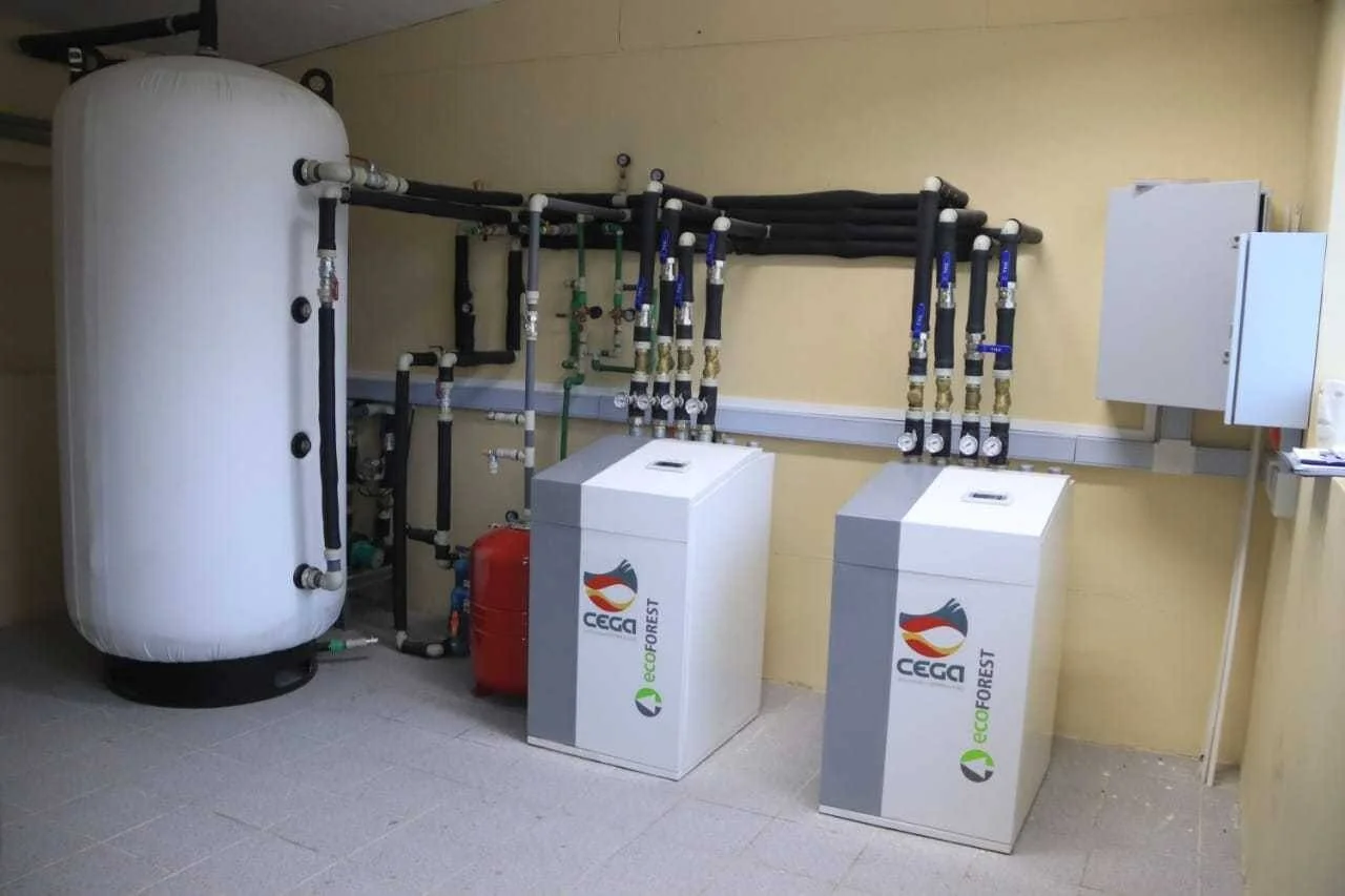 Sala técnica con dos unidades de bomba de calor geotérmica Cega Ecoforest conectadas a tuberías y un acumulador de inercia cilíndrico.