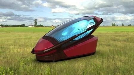 Cápsula futurista de color rojo con tapa transparente azul abierta, posada sobre un campo verde bajo un cielo nublado.