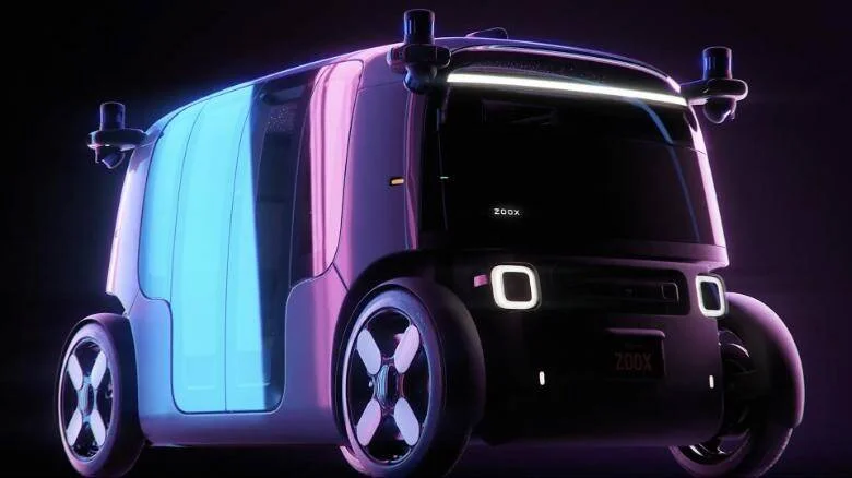 Prototipo de vehículo autónomo eléctrico de la marca Zoox, con diseño compacto, iluminación LED y sensores LiDAR en el techo.
