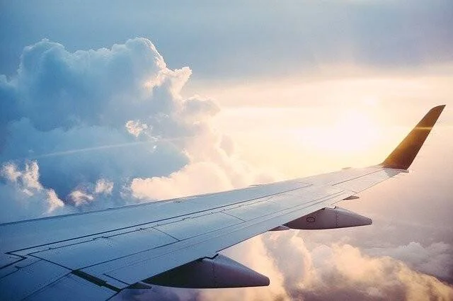 Vista desde la ventanilla de un avión mostrando el ala sobrevolando nubes iluminadas por el sol.