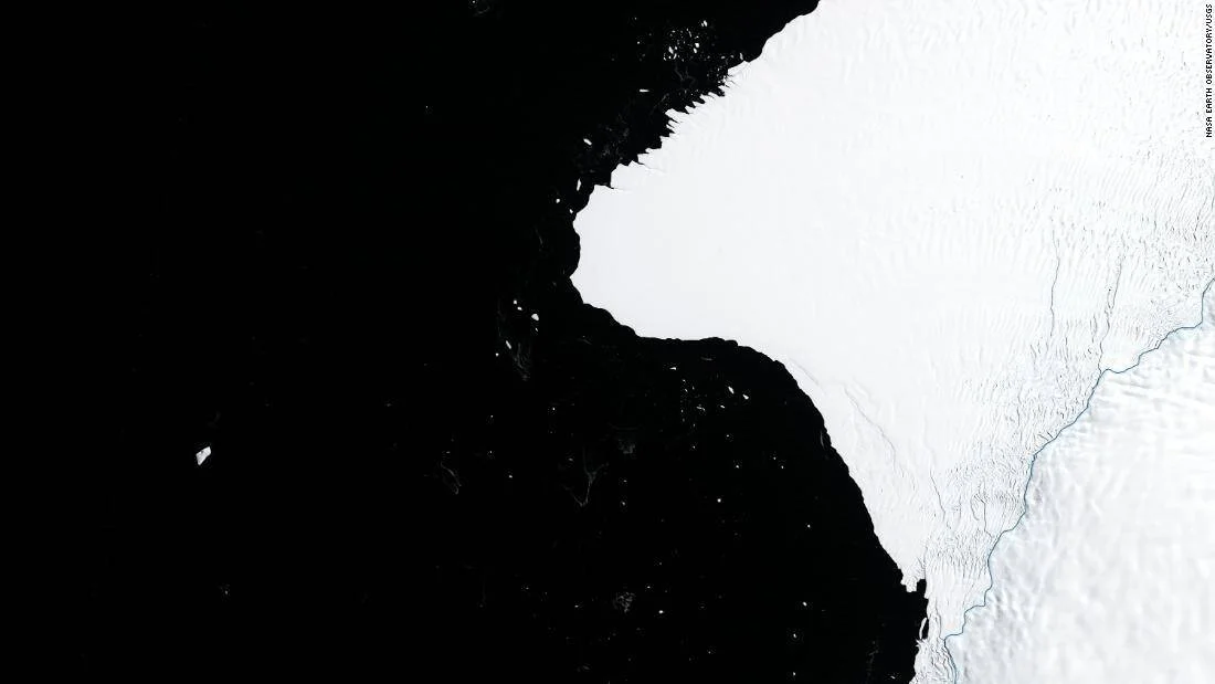 Vista satelital de NASA que muestra una plataforma de hielo antártica con una grieta y el océano oscuro a su izquierda.