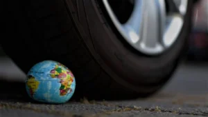 Pequeño globo terráqueo en el suelo a punto de ser aplastado por el neumático de un automóvil, simbolizando el impacto del transporte en el planeta.