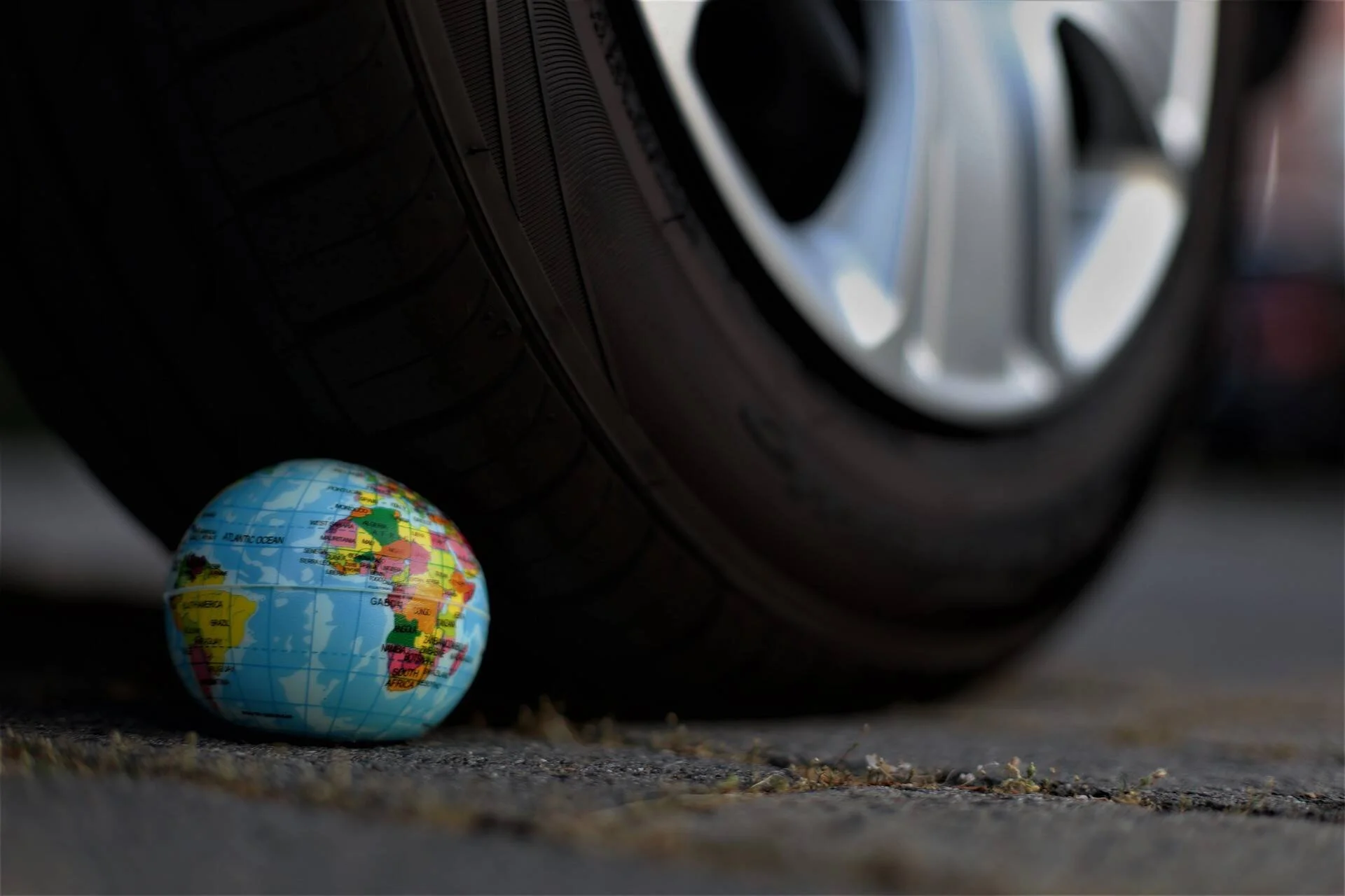 Pequeño globo terráqueo en el suelo a punto de ser aplastado por el neumático de un automóvil, simbolizando el impacto del transporte en el planeta.
