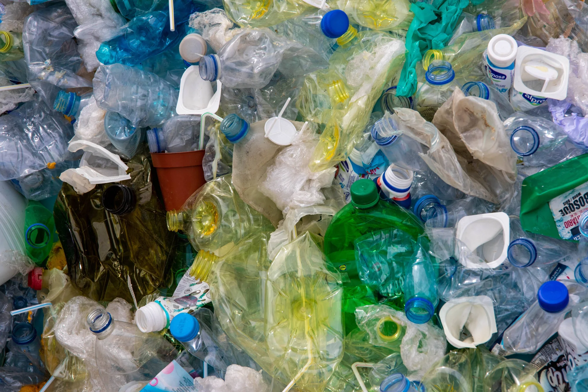 Gran acumulación de botellas, bolsas y envases plásticos de distintos colores y tamaños apilados sin clasificar.