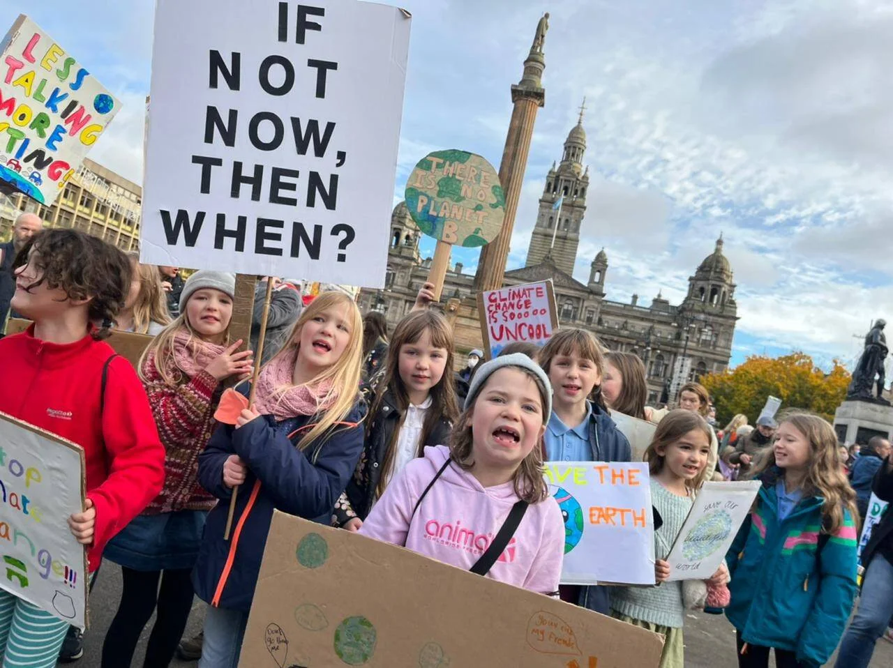 Grupo de niños porta pancartas sobre el cambio climático en una manifestación frente a un edificio histórico, exigiendo acción urgente.