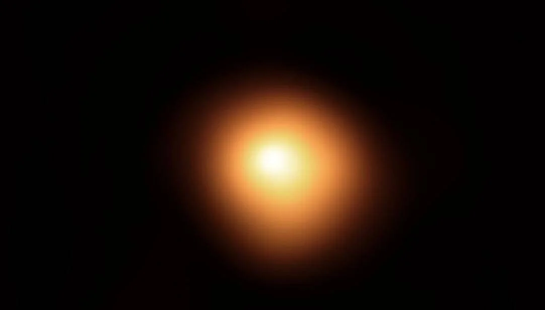 Estrella de color naranja-dorado con núcleo luminoso blanco rodeada de un halo difuso sobre fondo completamente negro.
