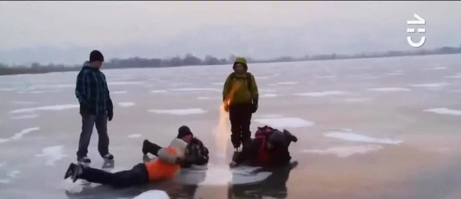 Varias personas sobre un lago congelado con grietas en el hielo; dos están tumbadas y dos de pie en aparente situación de riesgo.