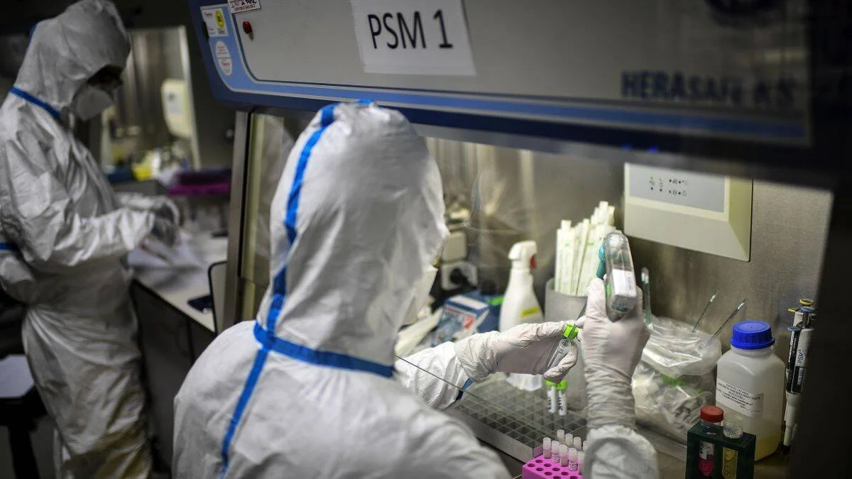 Dos investigadores con trajes de protección biológica manipulan muestras en una cabina de seguridad microbiológica PSM 1.