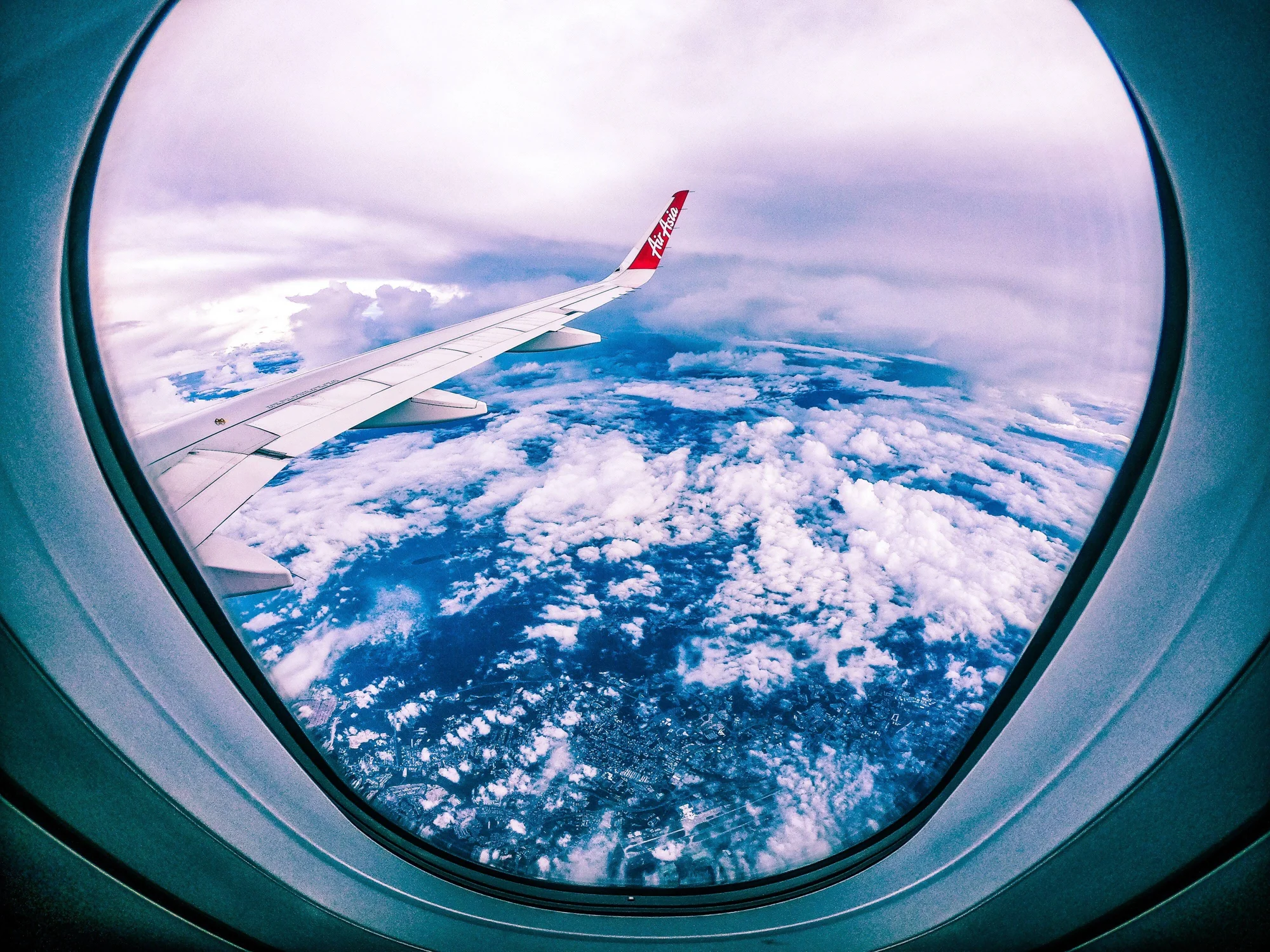 Ala de un avión de AirAsia vista desde la ventanilla de cabina, con nubes y tierra abajo.